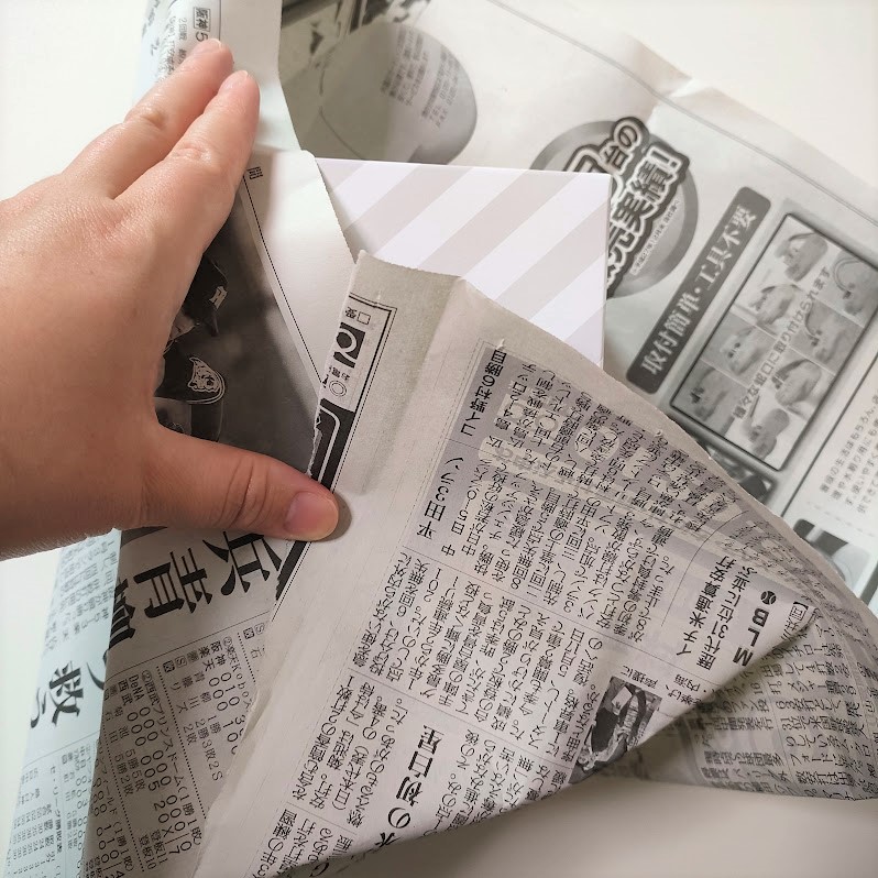 ダイソー「そのまま捨てられるサニタリーボックス」を新聞紙に包んでいるようす